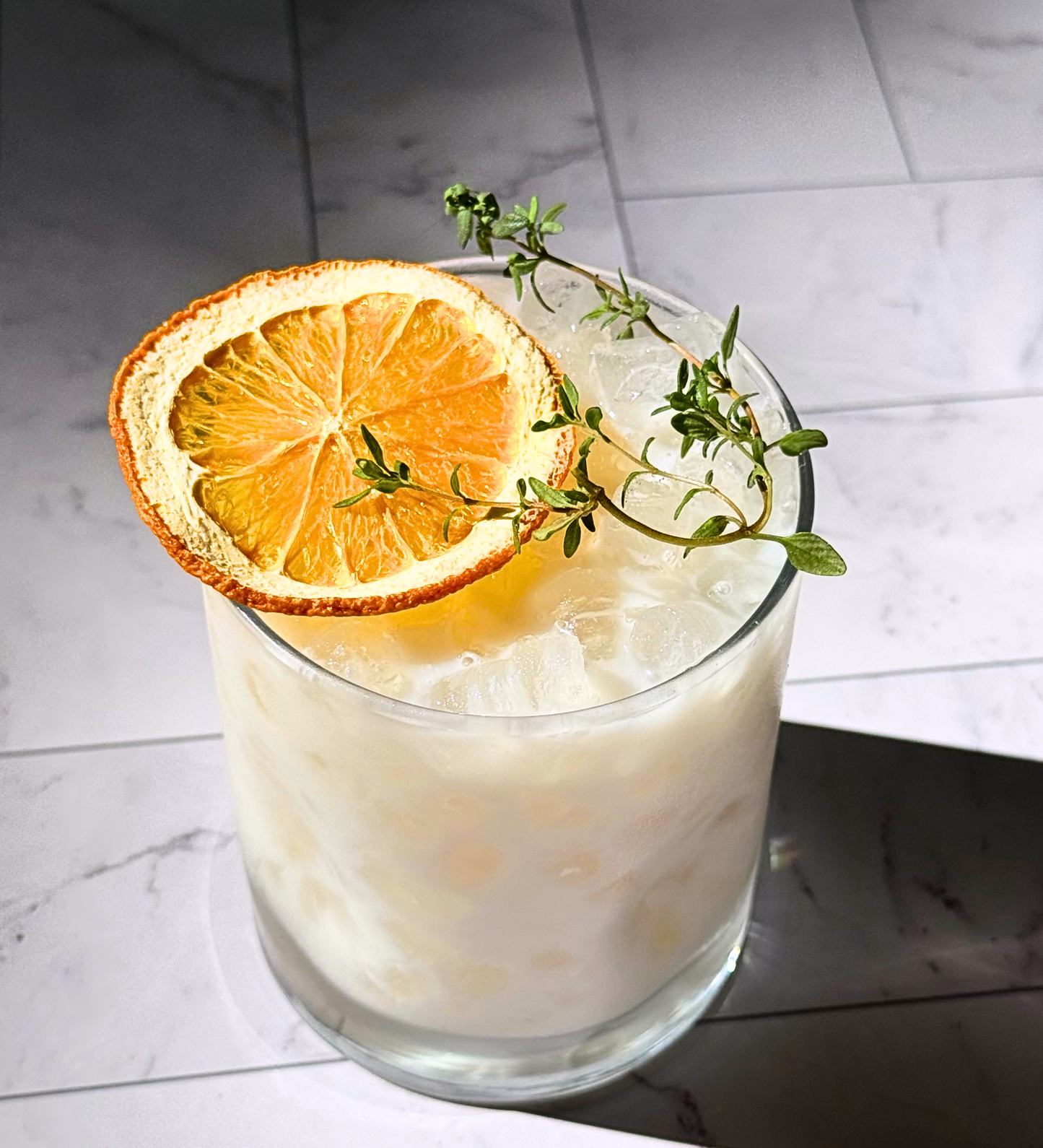 Cocktail with an orange slice and thyme garnish on a marble surface