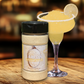 Jar of lemon-infused sugar next to a lemon-themed cocktail on a wooden surface.