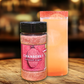 Jar of cranberry infused sugar next to a cocktail on a wooden surface with a blurred background