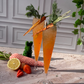 Two carrot-themed cocktails with garnishes on a stone surface with a decorative background.