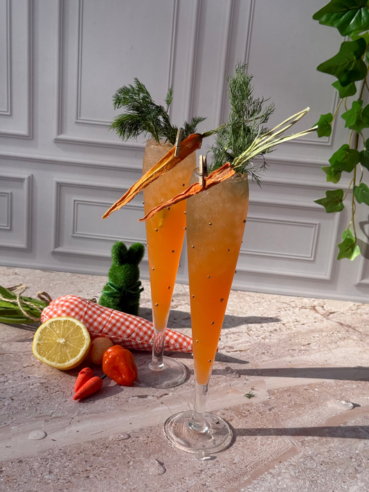 Two carrot-themed cocktails with garnishes on a stone surface with a decorative background.
