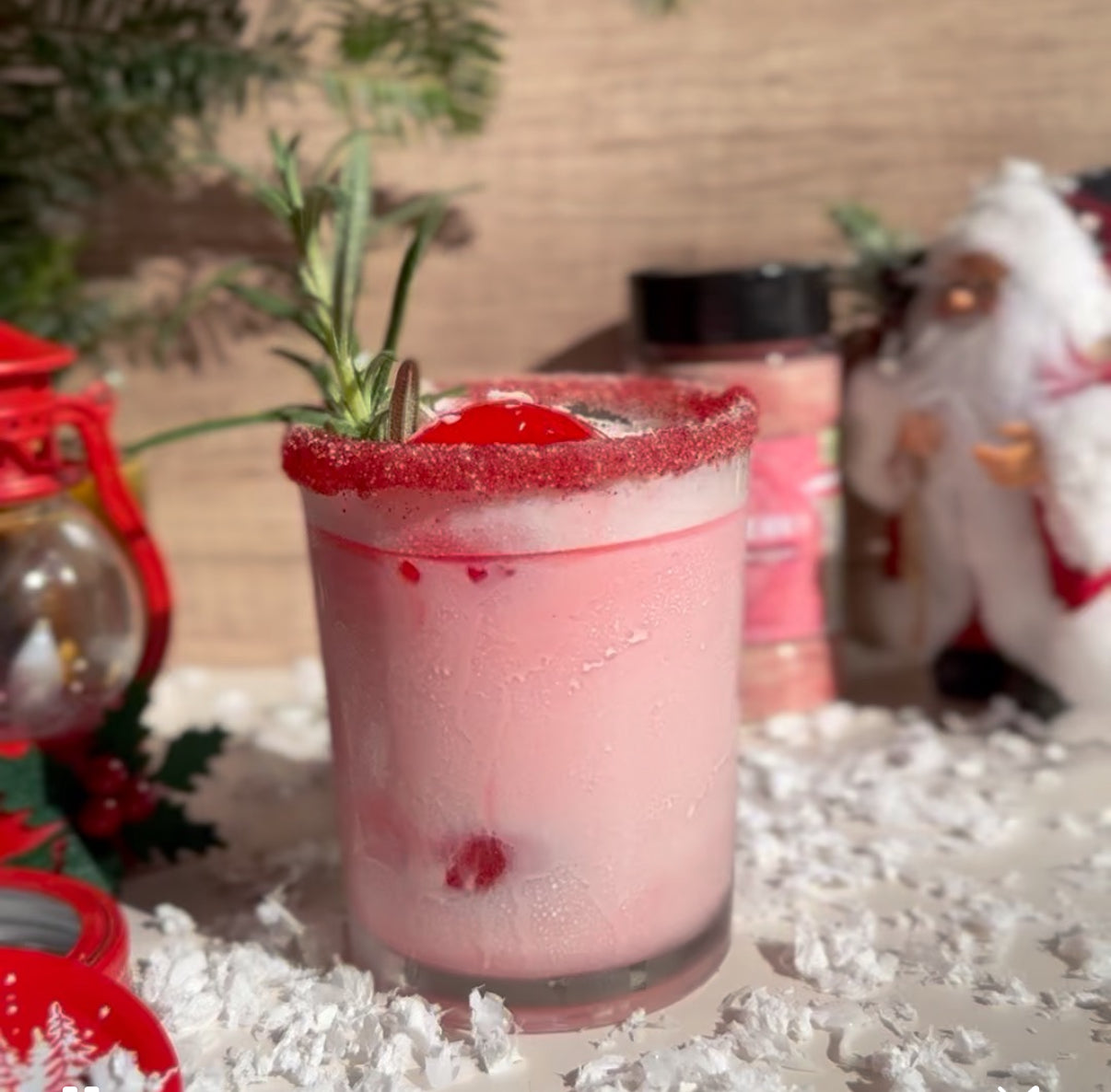 Pink cocktail with a sugared rim and rosemary garnish on a festive background.