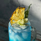 Blue cocktail with pineapple garnish on a marble surface