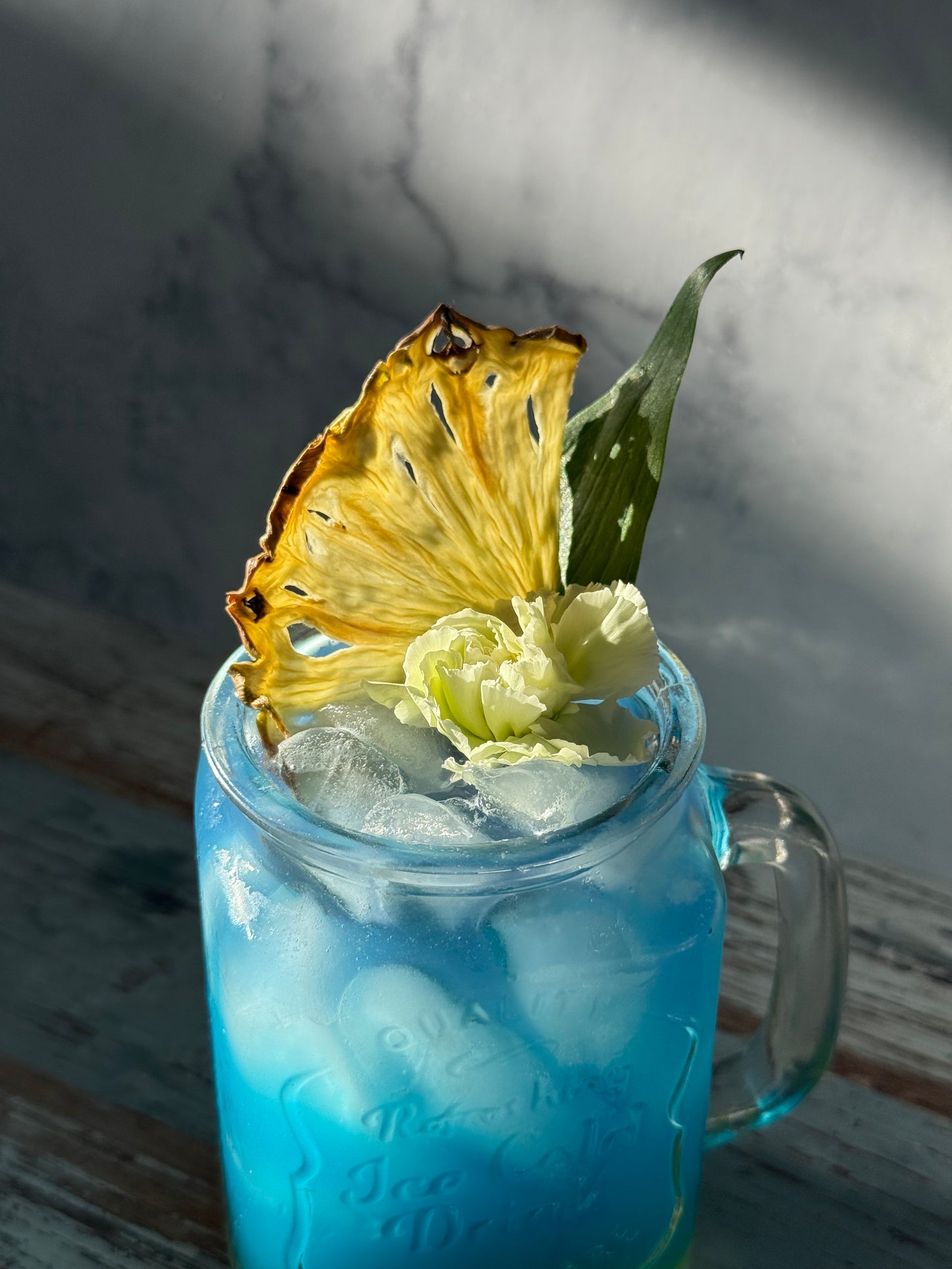 Blue cocktail with pineapple garnish on a marble surface