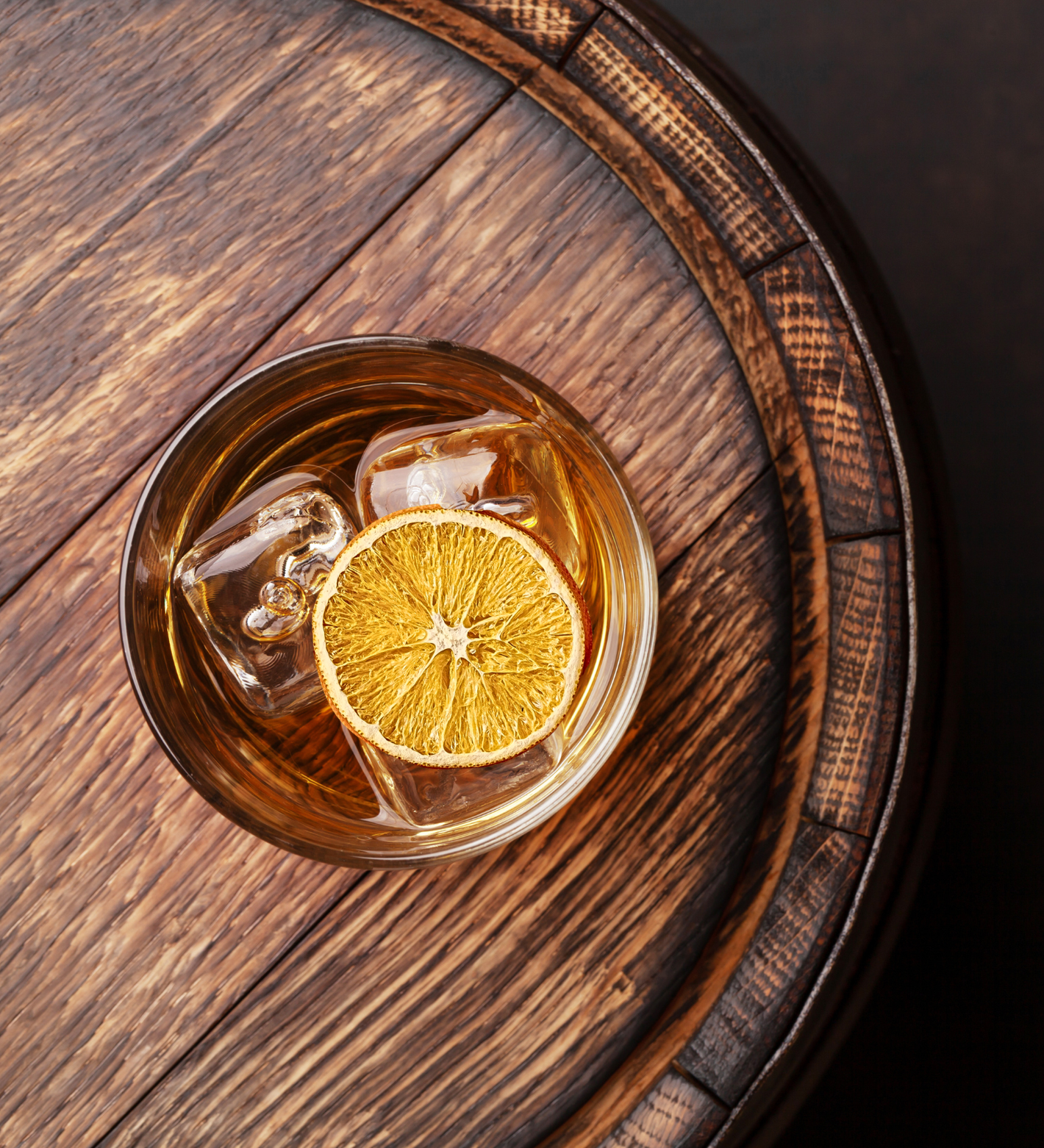 Glass of whiskey with a lemon wheel and ice cubes on a wooden barrel